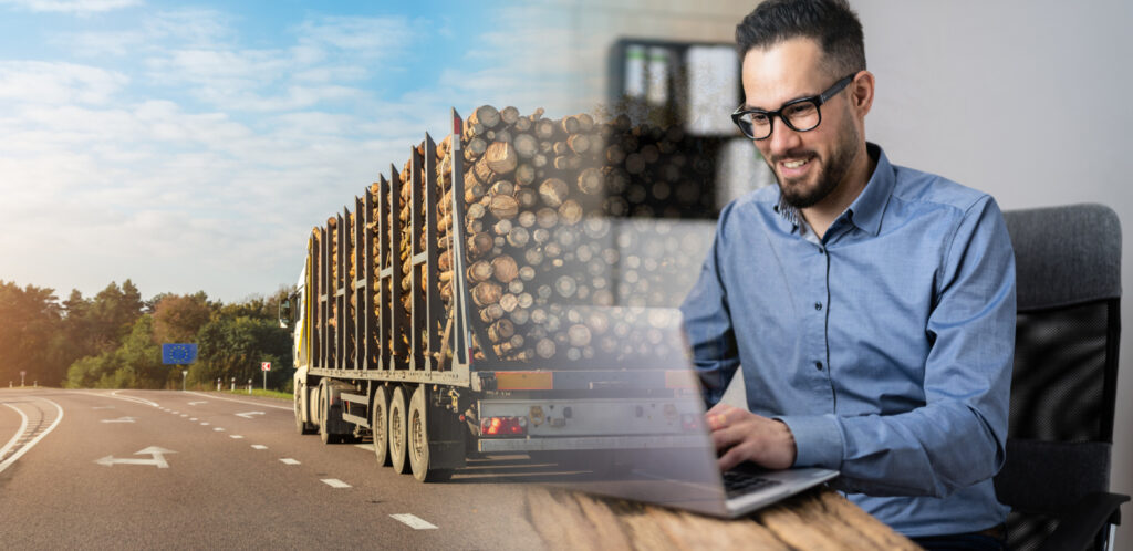 Glücklicher Mann sitz vor Laptop. Auf der Linken Seite ein Holztransporter mit Rundholz.